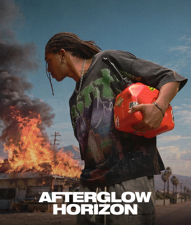 Model wearing a black DoubleCrazy graphic tee and carrying a red gas can beside a burning roadside motel in the Afterglow Horizon campaign.